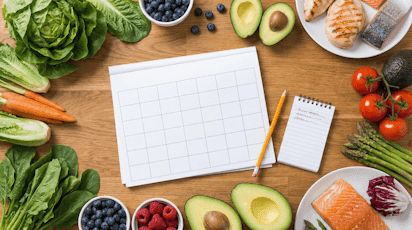 Meal planning — a calendar surrounded by fresh vegetables, salmon, avocado, and berries